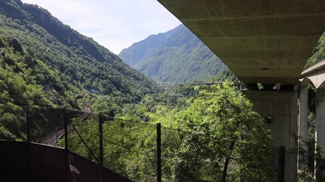 View of Gotthard Panorama Express SBB railway tracks winding through a lush green alpine valley with a river and mountain slopes in Lugano, Ticino, Switzerland.