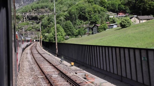 View of the Gotthard Panorama Express SBB train traveling along curved tracks through the lush landscape of Lugano, Ticino, Switzerland.