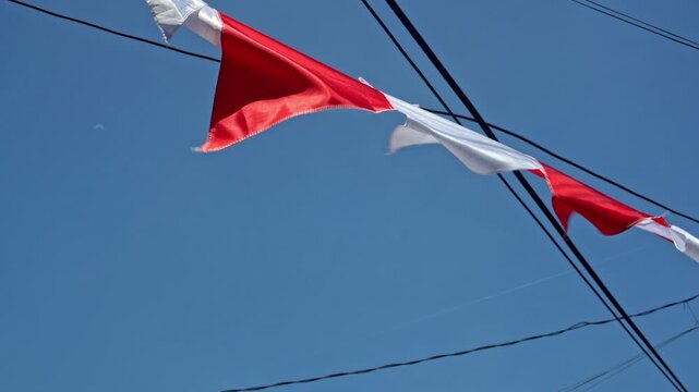 Red and white triangular festive flags waving against a clear blue sky, symbolizing national celebration and Indonesia independence day.