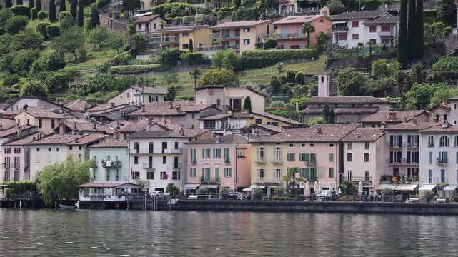 View of the historic lakeside village of Morcote with colorful buildings and lush green hills along the shore in Morcote, Ticino, Switzerland.