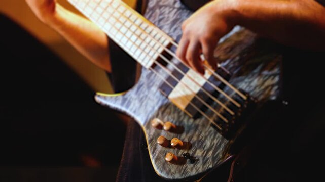Concert view of bass guitar player, bassist with vocalist and rock band performing in a club, male musician guitarist on stage with audience in crowded concert hall arena, hands on strings, live show