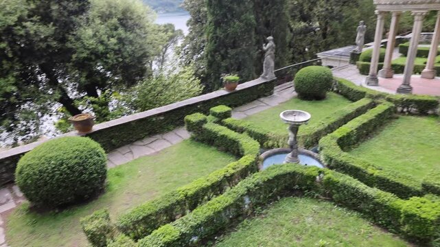 View of the classical rotunda with manicured hedges and statues in Parco Scherrer overlooking Lake Lugano in Morcote, Ticino, Switzerland.