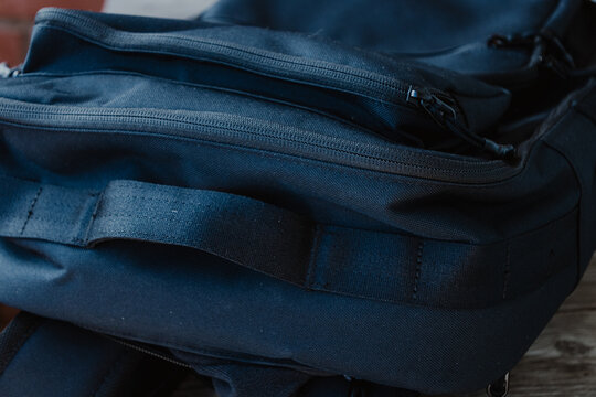A detailed close-up of a black backpack showing padded shoulder straps, zippered compartments, and durable fabric against a softly blurred brick background.