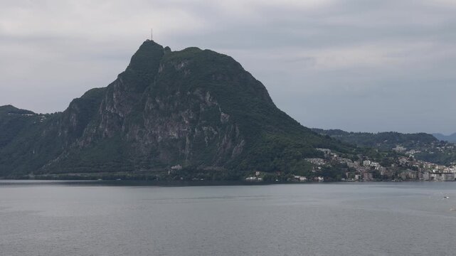 View of the lush green slopes of Monte Bre rising above the calm waters of Lake Lugano near the historic village of Gandria Lugano, Ticino, Switzerland.