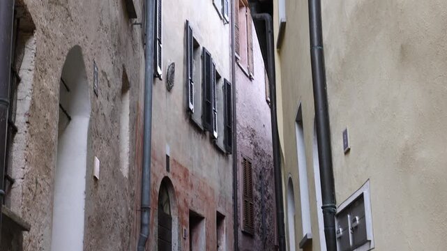 View of a narrow cobblestone alleyway lined with historic stone buildings and potted flowers in the village of Morcote, Ticino, Switzerland.