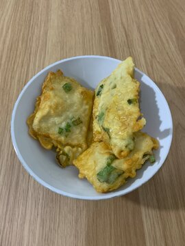 Traditional Indonesian fried tempeh with green onions in a white ceramic bowl on a wooden background, popular savory mendoan snack from Asian cuisine, crispy batter-coated fermented soybean cake.