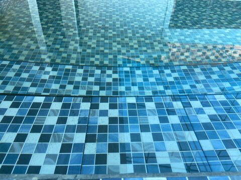 Top view of clear blue water in a swimming pool with mosaic tiles and soft sunlight reflections. Ideal for summer leisure and luxury spa concepts.