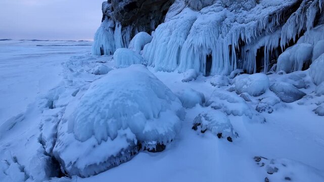 View of the frozen shoreline of Lake Baikal with dramatic ice formations on rocks and snow-covered ground in Khuzhir, Irkutsk Oblast, Russia.