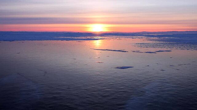 View of sunset over the frozen surface of Lake Baikal with calm ice and a vibrant orange sky in Khuzhir, Irkutsk Oblast, Russia.