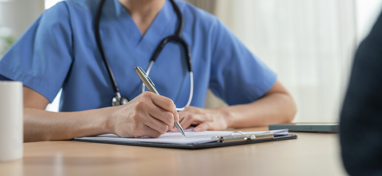 Healthcare consultation concept. Medical professional in blue scrubs writes patient notes on clipboard at clinic desk. Healthcare, doctor, medical, consultation, diagnosis.