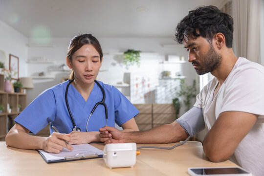 Healthcare professional measuring male patient blood pressure during medical checkup, monitoring vital signs while recording results for preventive care, health assessment, patient wellness.