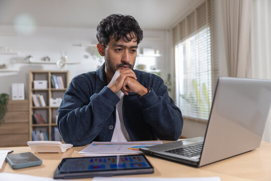 young man working from home with laptop, tablet and financial charts, analyzing business data and planning strategy in office for remote work, productivity and management.