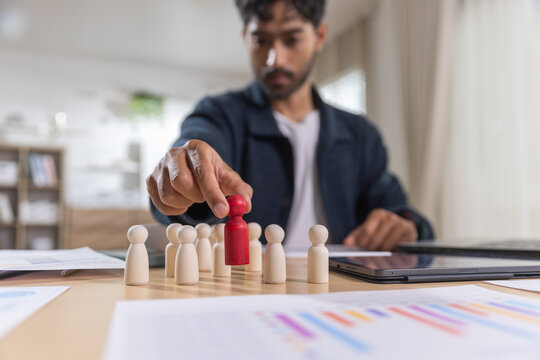 Leadership concept. Businessman selects red figure from team at an office desk, symbolizing recruitment and talent management. Leadership, recruitment, team, talent, management.