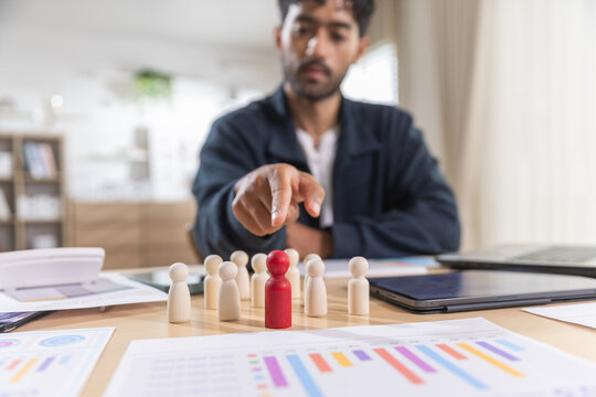Leadership concept. businessman points to red figure standing out from team at an office desk, symbolizing recruitment and talent selection. Leadership, recruitment, talent, team, hiring.