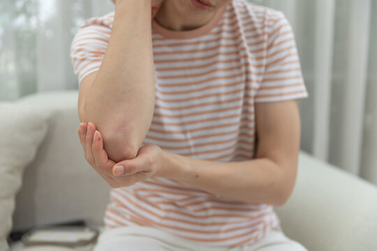Elbow pain concept. women holding sore elbow while sitting at home, showing joint discomfort and possible strain. Elbow pain, woman, joint, discomfort, healthcare.