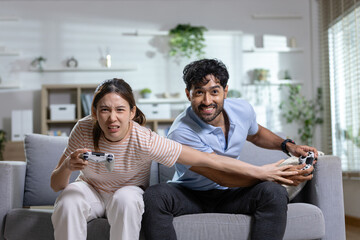 Gaming couple concept. competitive couple plays video games with controllers on sofa at home, showing fun and friendly rivalry. Gaming, couple, competition, entertainment, lifestyle. © eakgrungenerd