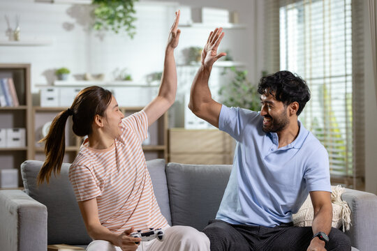 Gaming celebration concept. A happy couple shares a high five after playing video games with a controller on a sofa at home. Gaming, celebration, couple, victory, teamwork.