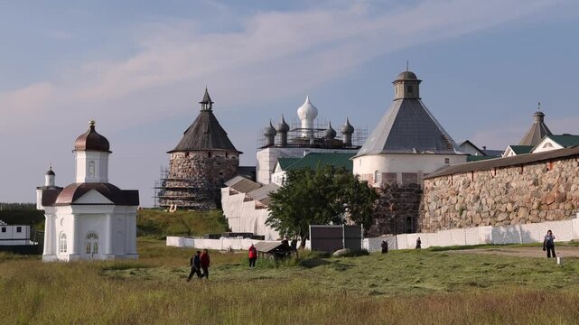 View of the historic Solovetsky Monastery with stone walls, towers, and church domes under a clear sky, with people walking on the grounds in Solovetsky, Arkhangelsk Oblast, Russia.