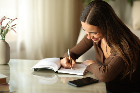 Woman writing in paper agenda using pen on a coffee table