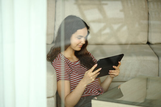 Teenage girl watching media on tablet through window
