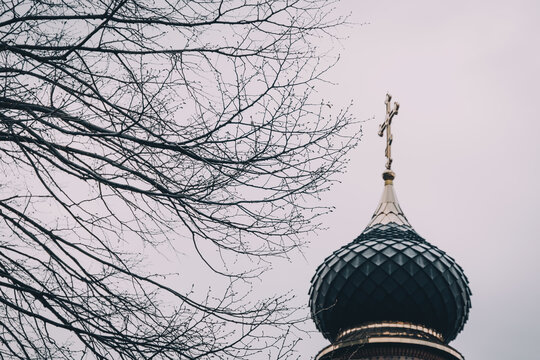 Orthodox church dome and cross reaching towards an overcast winter sky through a tangle of bare branches, symbolizing faith and spirituality
