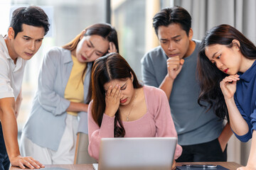 Fototapeta premium Stressed young asian business team dealing with work pressure, conflict and difficult problems together around laptop in office