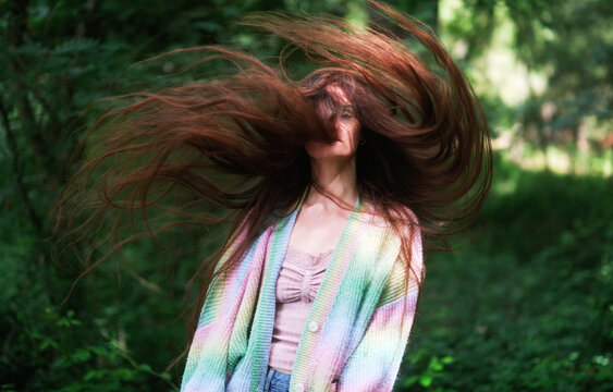 Young brunette woman swings her exceptionally long hair through the air in a green forest creating a dynamic playful portrait filled with energy and motion