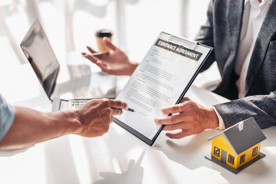 Real estate professional and client reviewing property contract and mortgage documents for home purchase and financing in office