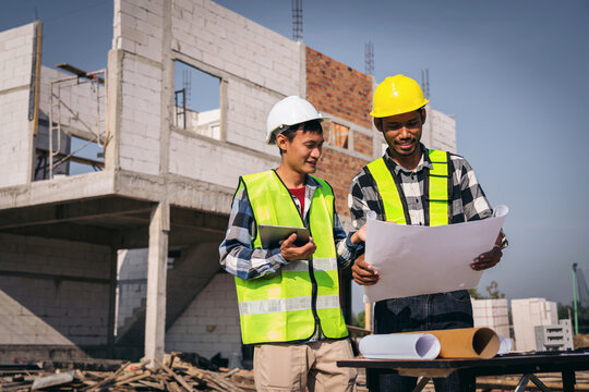 Two Young Asian Construction Workers Reviewing Blueprints at Con