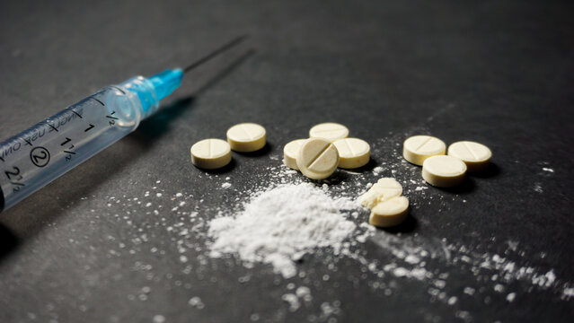 White illegal drugs in powder and pill form with a syringe on black background. Misused drugs concept. 