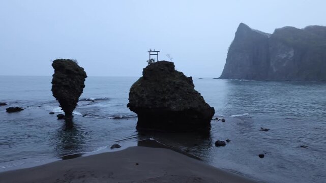 View of the iconic sea stack with a torii gate at Cape Kamui, set against dramatic coastal cliffs and the sea in Esashi, Hokkaido, Japan.