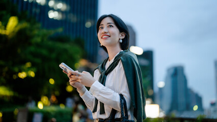 Naklejka premium Business asian woman relax using smartphone social network communication metropolis city building background