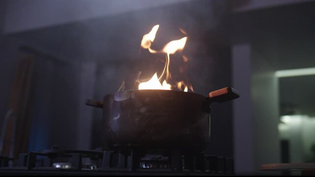 Flame Bursting Out of a Cooking Pot on a Gas Stove in a Dark Kitchen, Dangerous Kitchen Fire Accident Close Up, Cooking Oil Catching Fire Emergency Concept, Stovetop Flambe Blaze Warning Footage