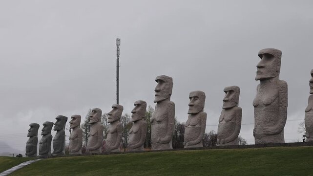 View of a row of stone Moai statues standing on a grassy hill under a cloudy sky in Sapporo, Hokkaido, Japan.