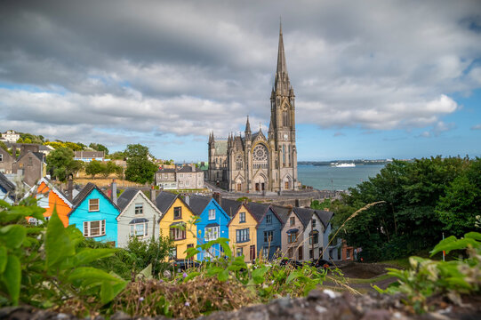St. Colman's Cathedral and colorful houses in Cobh, County Cork, Ireland. Neogothic St. Colman's Cathedral rising above row of vibrant, colorful Victorian houses on steep hill in harbor town of Cobh.