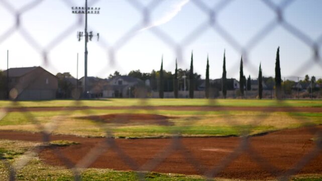 Empty baseball field behind chain link fence during sunny day.