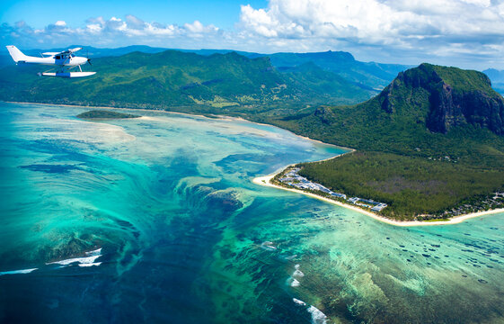 An underwater waterfall off the island of Mauritius, a seaplane flies over the ocean against a backdrop of a coral reef. Aerial view of Le Morne Mountain.