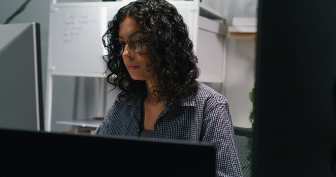 Latin woman investigates a flagged network event in an ops bay, isolating systems and preparing incident notes.