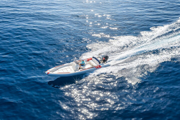 Obraz premium Aerial top view of a RIB motorboat with outboard engine cruising with high speed over the ocean