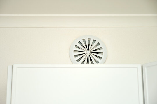 White round ventilation grille on wall above kitchen cabinet. Kitchen exhaust vent for air circulation and freshness. Modern interior design and ventilation system concept.