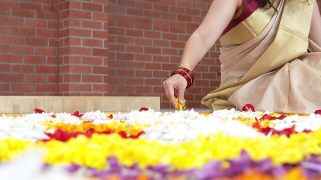 View of a woman wearing a traditional saree creating a vibrant floral Pookalam rangoli on the floor during the Onam festival in India.