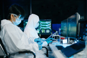 Professional scientists in protective suits collaborating on research, examining microscope...