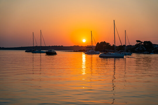 Sailing yachts anchored in a calm bay during a colorful summer sunset over the sea. Peaceful evening, golden hour, coastal travel destination and relaxing sailing lifestyle.