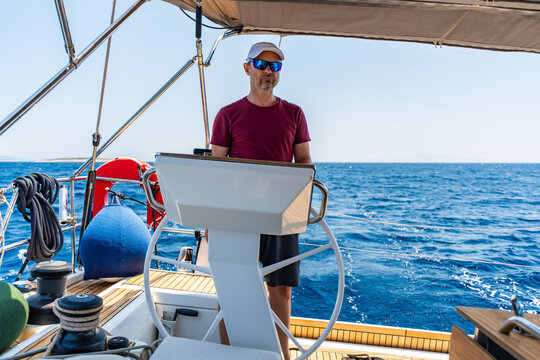 Experienced sailor steering a sailing yacht during an offshore passage at sea. Seamanship, navigation skills, confident boat handling and active cruising lifestyle.