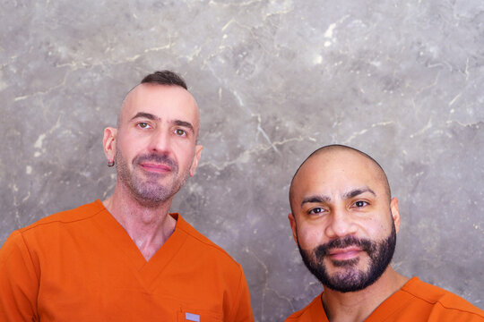 Two men in orange scrubs smiling, representing beauty salon staff or medical professionals