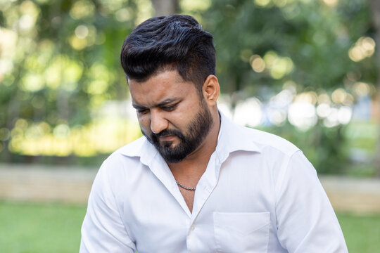 young adult south asian man portrait with sad and unhappy facial expression, head and shoulder shot, outdoor scene