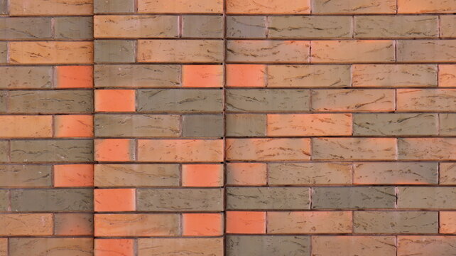 A section of modern brickwork with a variegated texture. The horizontal courses consist of clinker bricks in shades of terracotta, brown, orange, and grey-green. The joints are neat and fine.