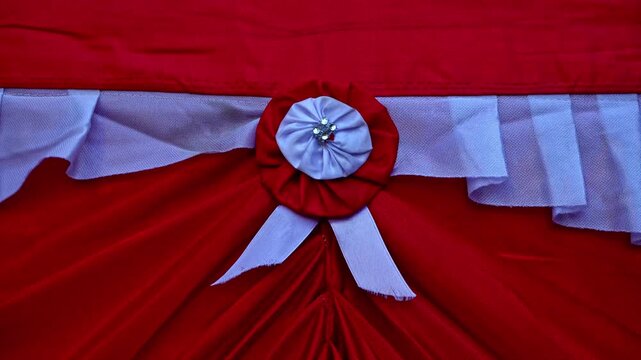 Red and white decorative fabric arrangement featuring pleated drapes and a rosette flower ornament for national independence day celebration.