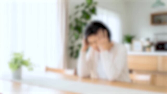 ぼかし背景素材: 自宅のテーブルで頭を抱えて悩むシニア女性のイメージ　高齢者の悩み