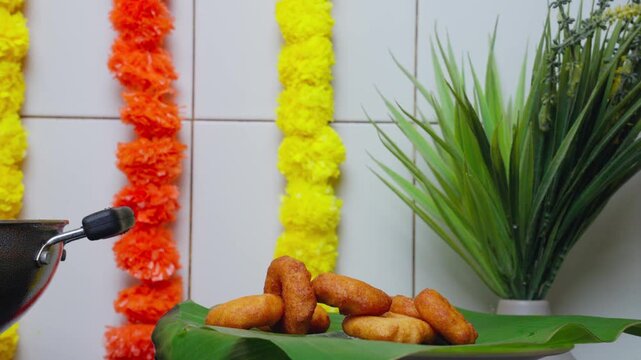 Golden vada dropping slowly on a banana leaf for a festive feast with vibrant marigold decorations in the background in Vijayawada, Andhra Pradesh, India.
